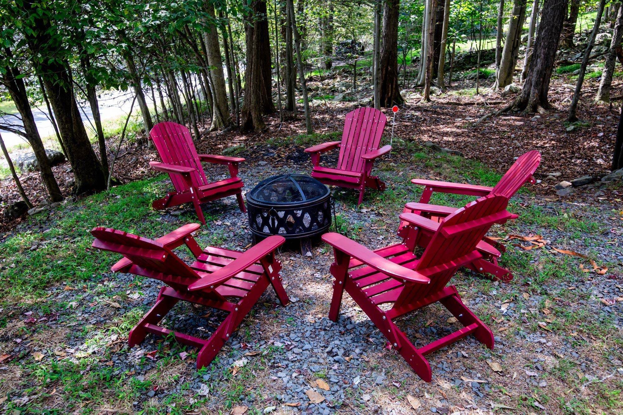 Outdoor fire pit ringed by red Adirondack chairs in the wooded Pocono setting